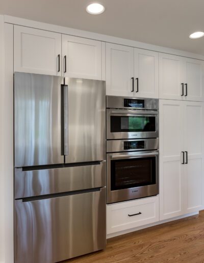 A white kitchen with stainless steel appliances and hardwood floors.