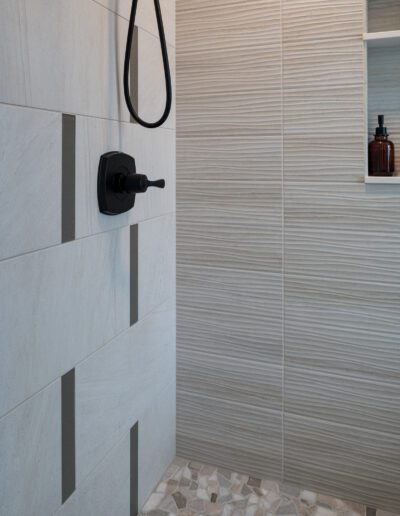 A tiled shower with a shower head and shelves.