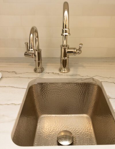 A sink with two faucets and a cup of coffee.