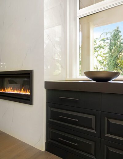 A fireplace in a bathroom with black cabinets and a window.