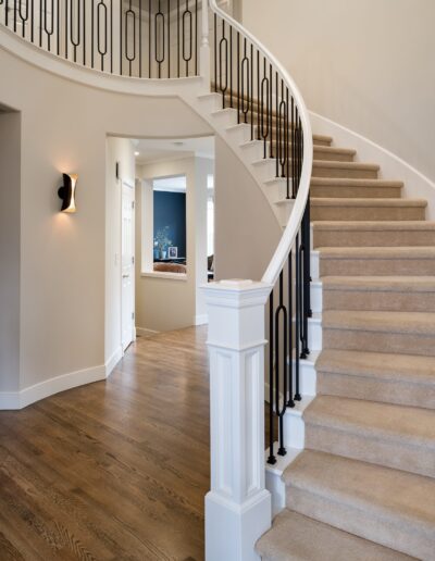 Elegant interior of a home showing a curved staircase with a wooden banister and wrought-iron balusters, leading up from a hallway with hardwood floors.