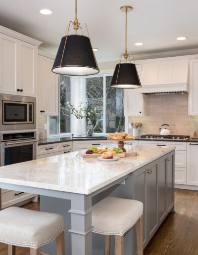 Modern kitchen interior with white cabinetry, a central island with stools, stainless steel appliances, and hanging black pendant lights.