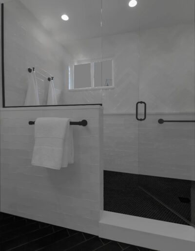 Modern bathroom with white subway tiles, black herringbone floor, glass shower door, and hanging white towels.