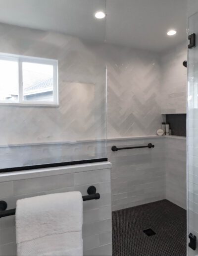 Modern bathroom with white herringbone tiles, a glass shower enclosure, and a freestanding tub near a window.