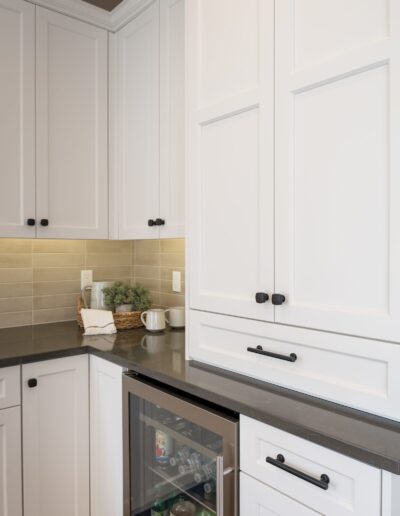 A modern kitchen corner featuring white cabinets, black countertops, and a built-in glass-front mini fridge.