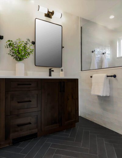 Modern bathroom with dark wood vanity, double sinks, black-framed mirrors, and a walk-in shower with glass door.