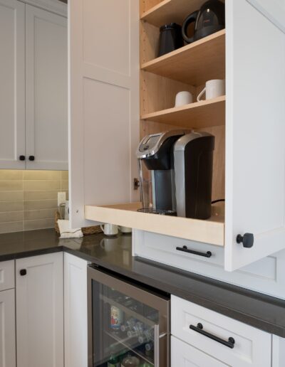 A modern kitchen corner with white cabinets, a built-in coffee machine on the counter, and an open cupboard displaying assorted dishes.