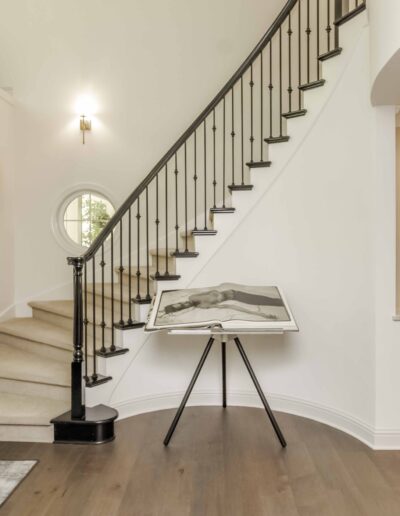 A curved staircase with a black railing and a large book on a stand. White walls and artwork decorate the space.