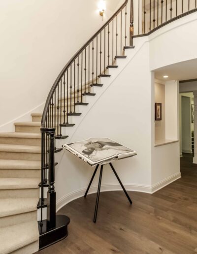 Spacious foyer with a curved staircase, circular window, large photo on a stand, and view of a dining room with a set table and chairs.