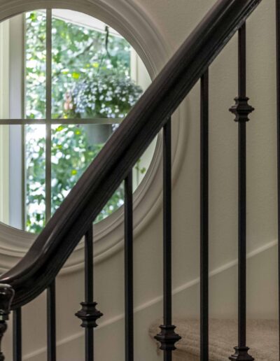 Circular window with a view of greenery, next to a staircase with black iron railings and carpeted steps.