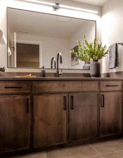 Modern bathroom with a large mirror above a dark wood vanity featuring a black faucet. A potted plant and soap dispenser are on the countertop, with a towel on the right side.