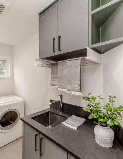 Laundry room with a gray countertop, sink, washing machine, overhead cabinets, a towel hanging, and a potted plant.