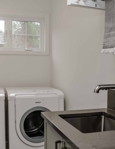 A laundry room with a washer and dryer, a gray countertop, a sink with a silver faucet, gray towels, and a small window.