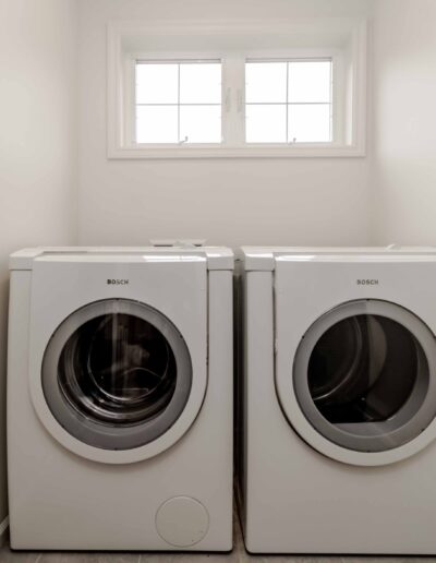 A laundry room with a front-loading washing machine and dryer side by side under a small window.