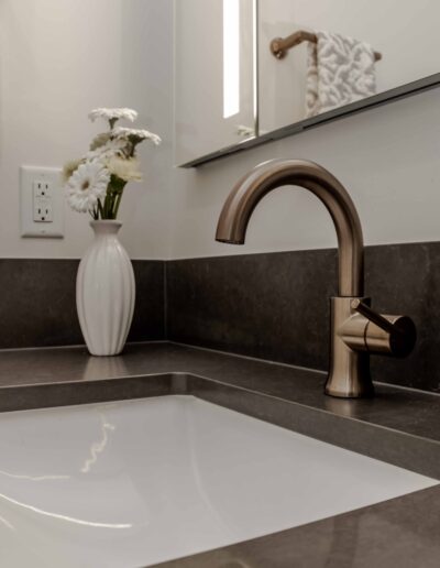 A modern bathroom sink with a metallic faucet, white countertop, and a vase with white flowers in the background.