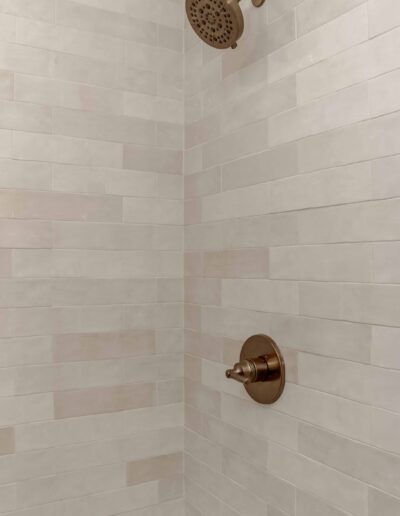 A tiled shower wall with a bronze showerhead and a matching control valve.